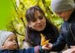 Joyful family moment in park with kids playing among colorful autumn leaves.