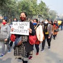 Women in masks hold signs at a job security protest on an urban street, demanding change.