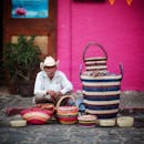 An elderly street vendor in Tepoztlán, Mexico, selling colorful handmade baskets on a vibrant street.